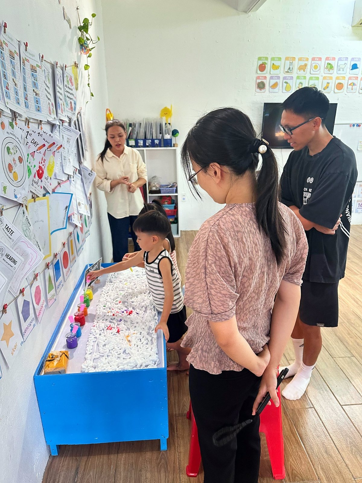 An Early Years student at a foam tray with colour droppers as parents watch
