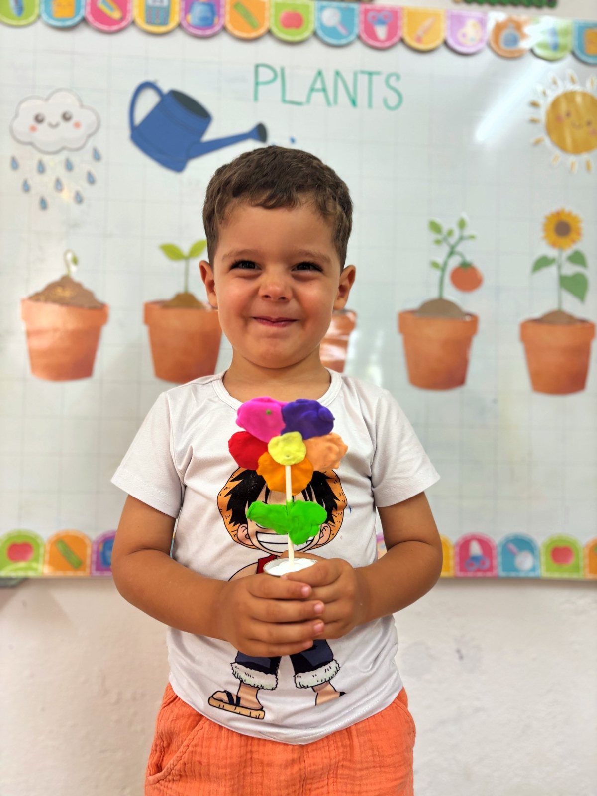 A Nursery boy holding up the play dough flower he made in a little pot