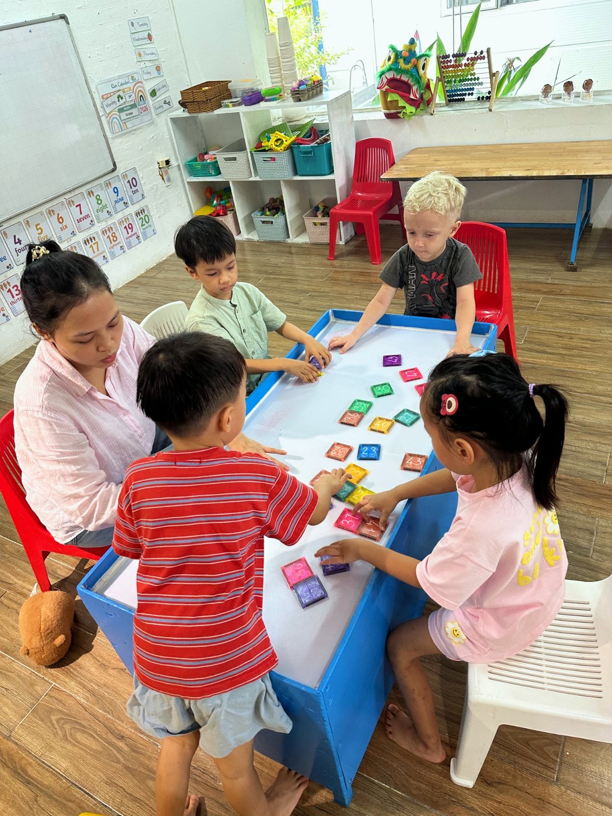Kindergarten children laying coloured number tiles on the light table with their teacher