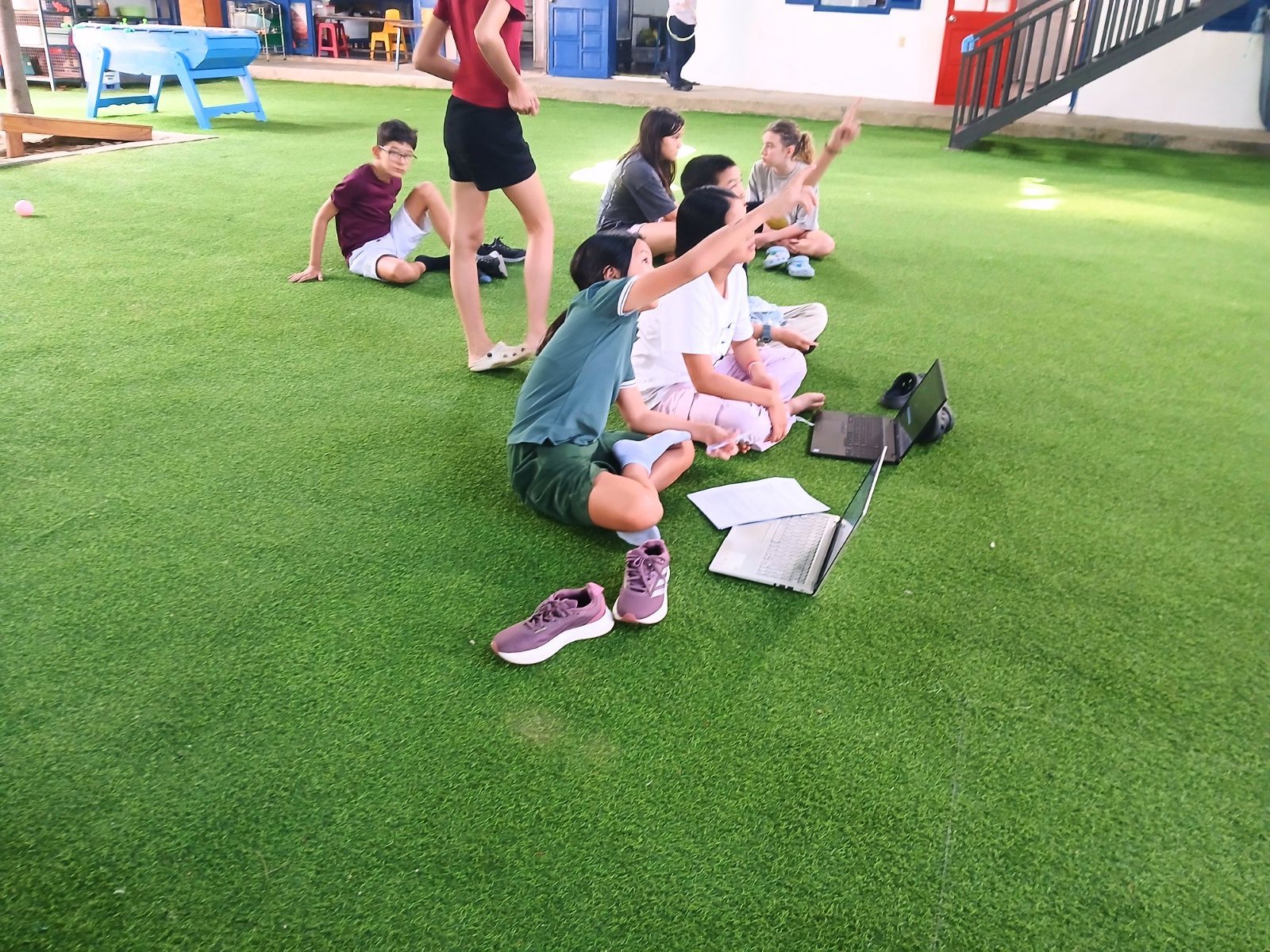 Year 7 students on the grass with laptops, pointing up at the balcony drop