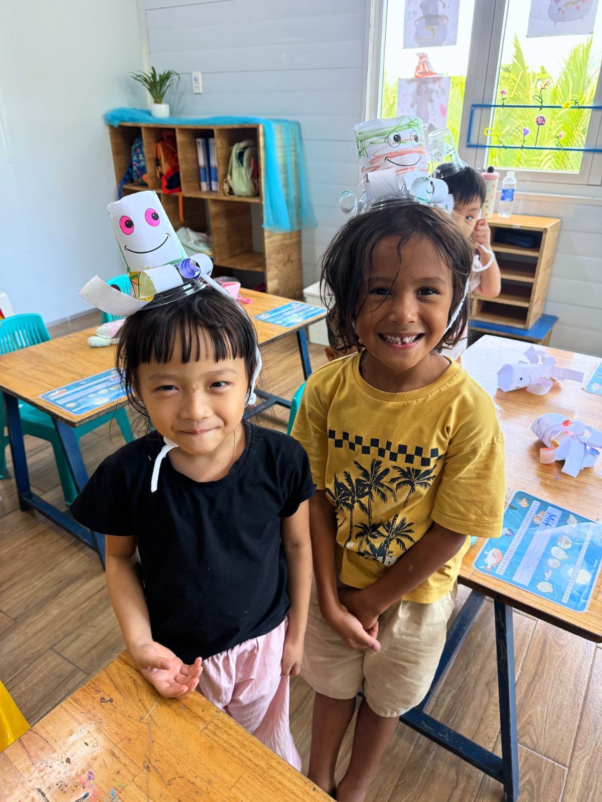 Two Year 1 girls grinning in the paper hats they made