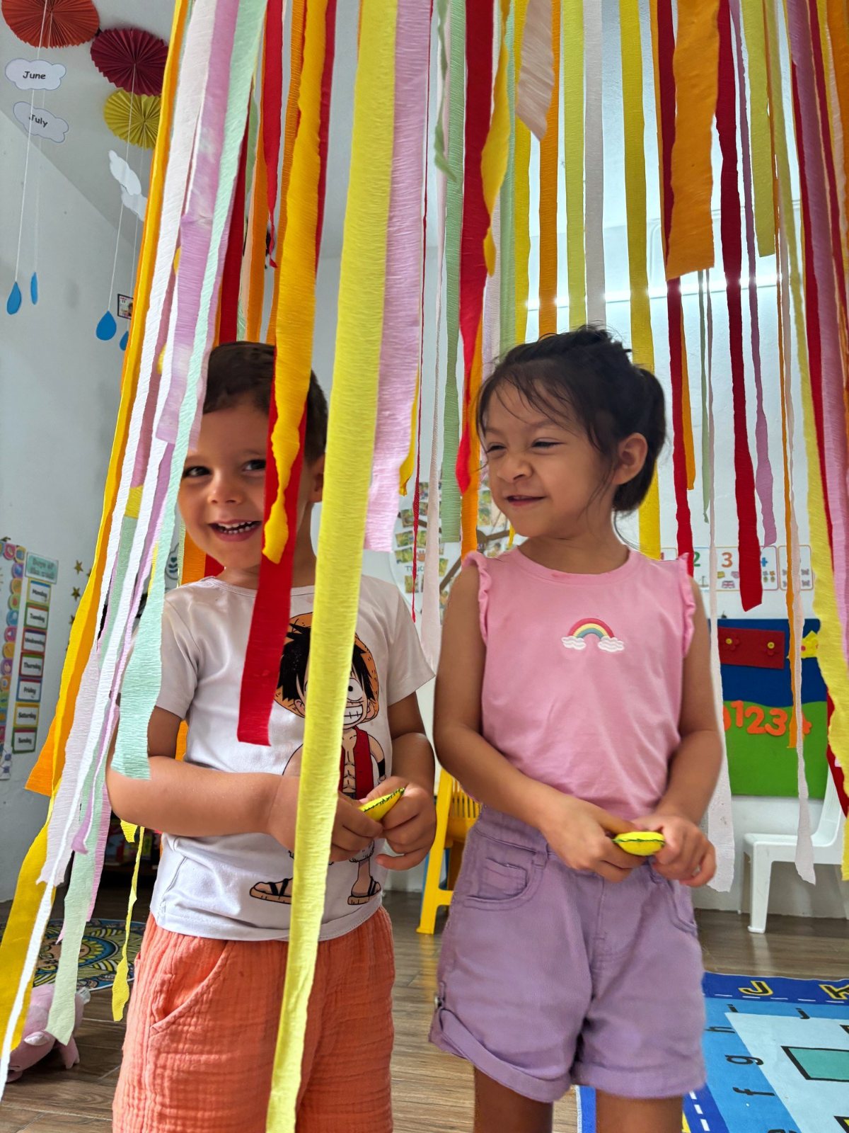 Two Nursery children smiling through a curtain of crepe paper streamers