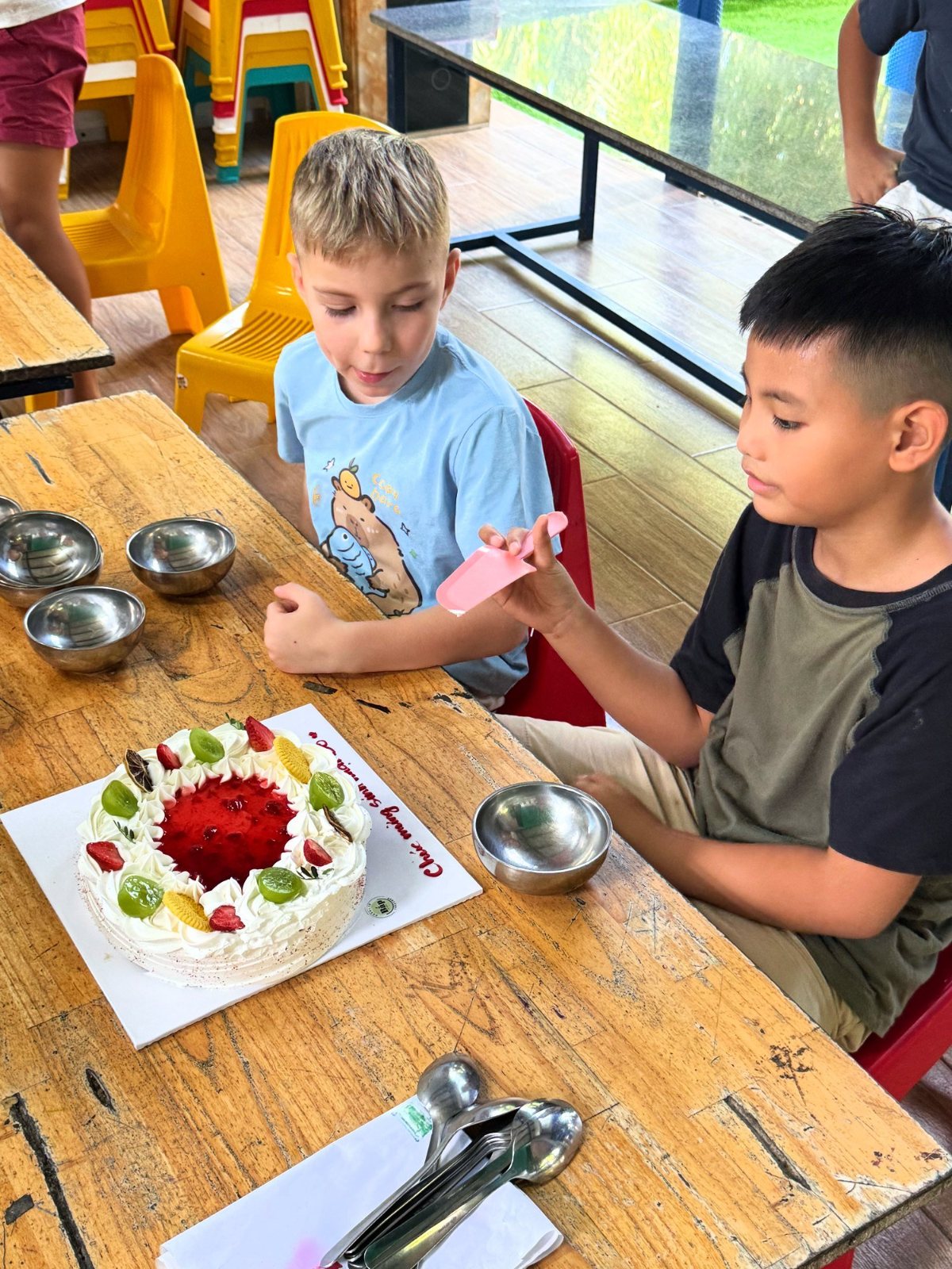 Year 5 students waiting with spoons beside a fruit-topped birthday cake