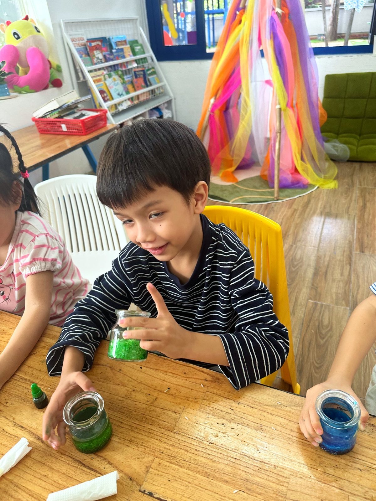 A Kindergarten child pointing at his jar of coloured water for the roots experiment
