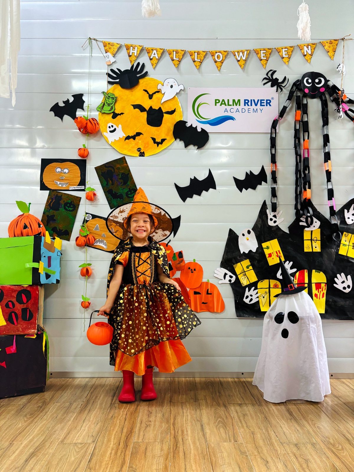 A Nursery child in a witch costume standing at the Halloween wall