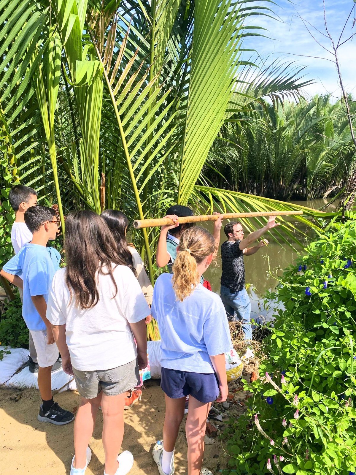 Year 7 students carrying their bamboo tide pole to the river through the palms