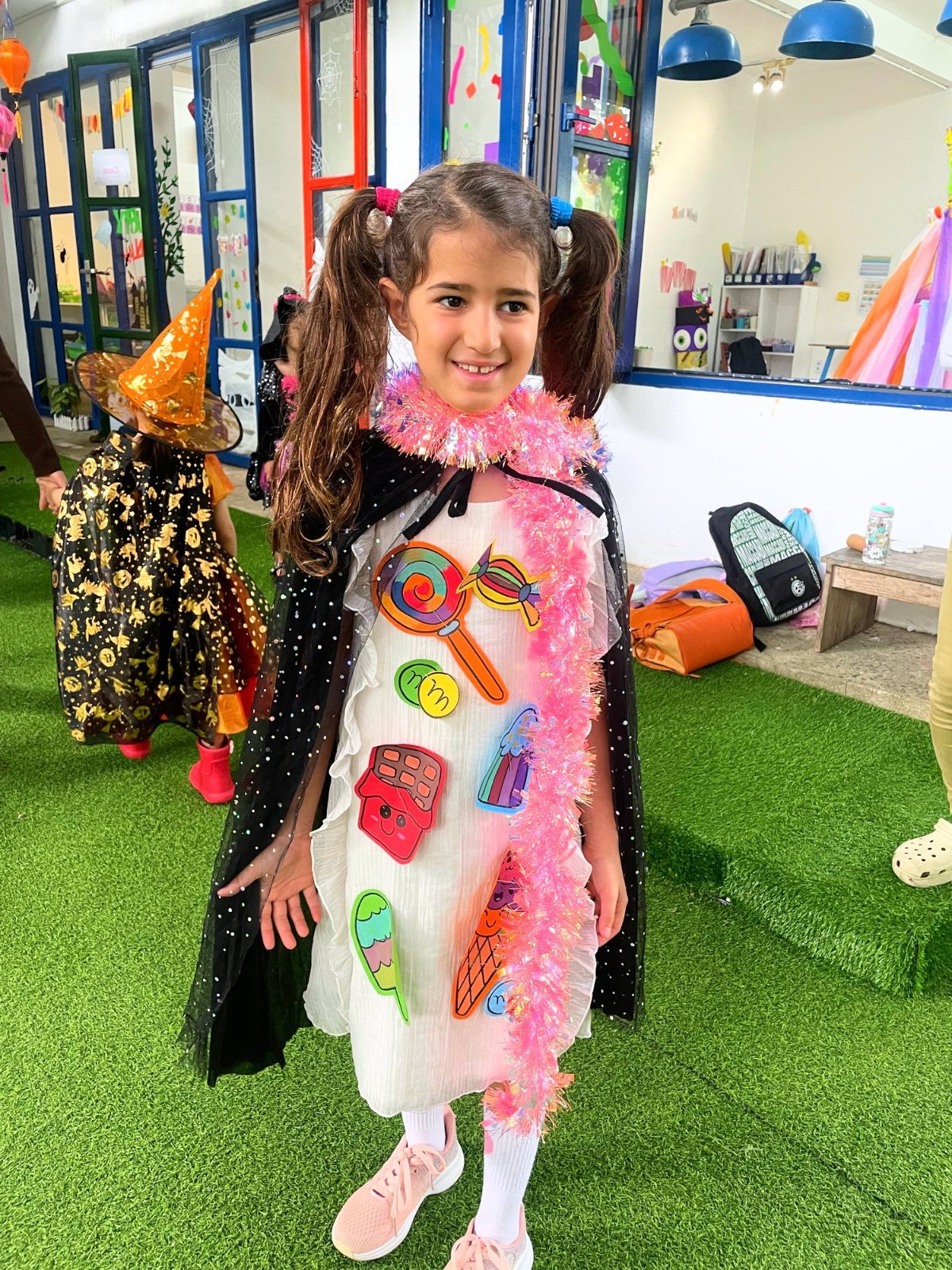 A student smiling in a cape covered in sweet-wrapper cut-outs on Halloween