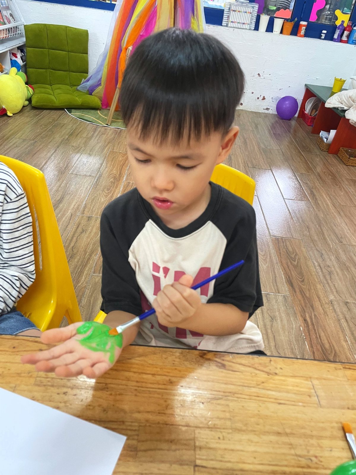 A Kindergarten child painting his palm green to make Halloween zombie fingers