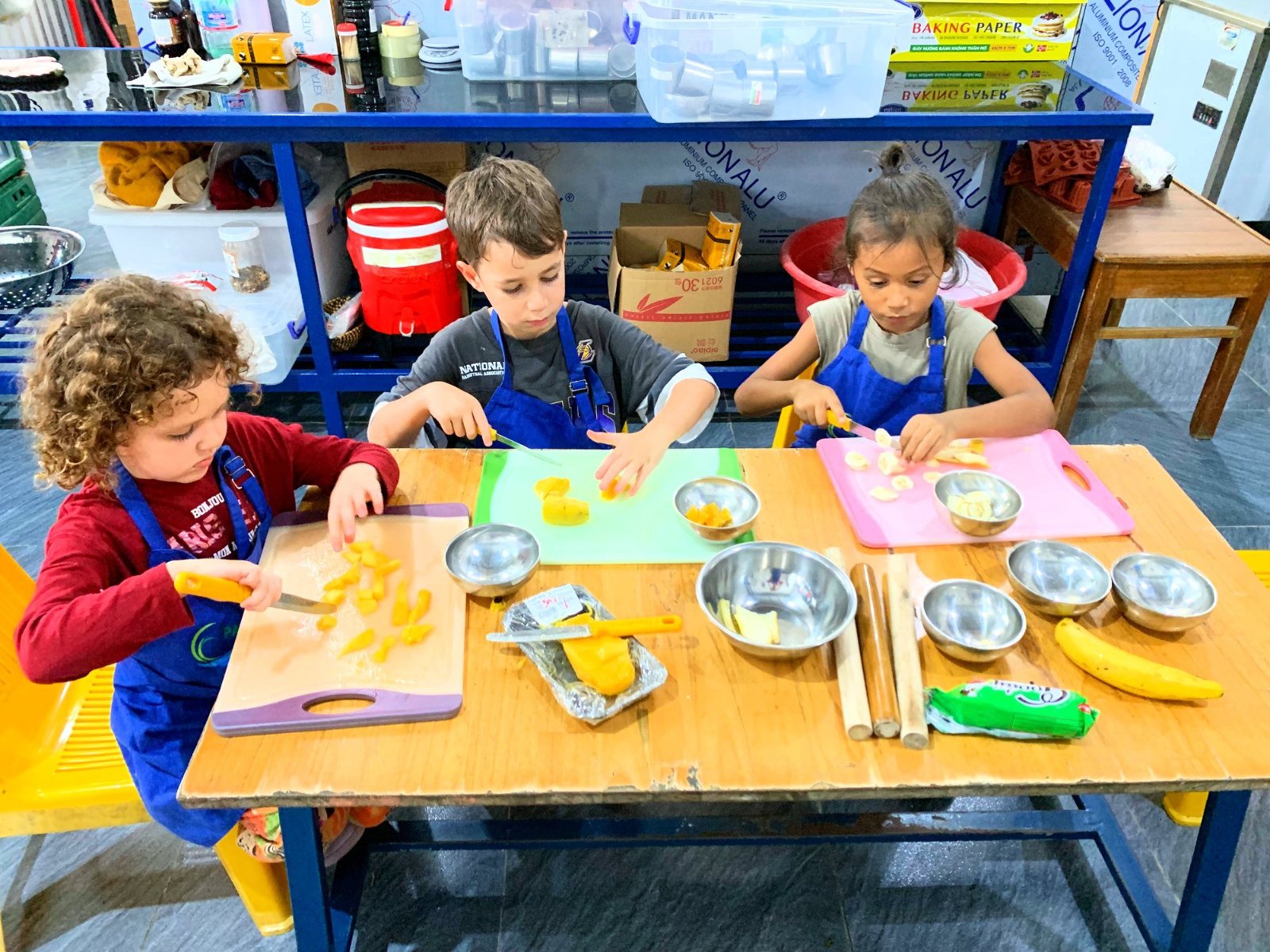 Year 1 children in aprons cutting mango and banana in the kitchen